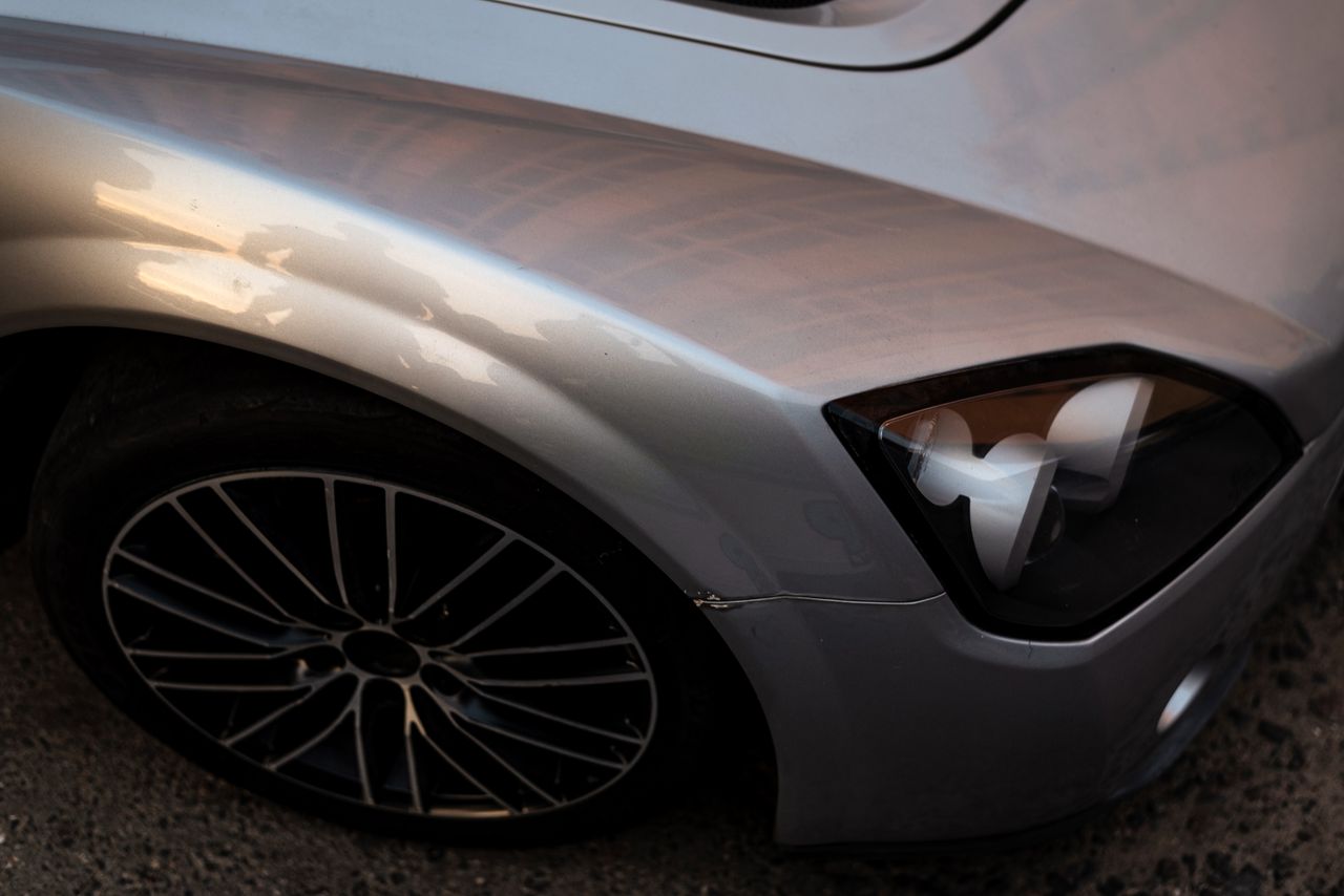 Detailed view of a silver car's headlight and wheel with a smooth metallic finish.