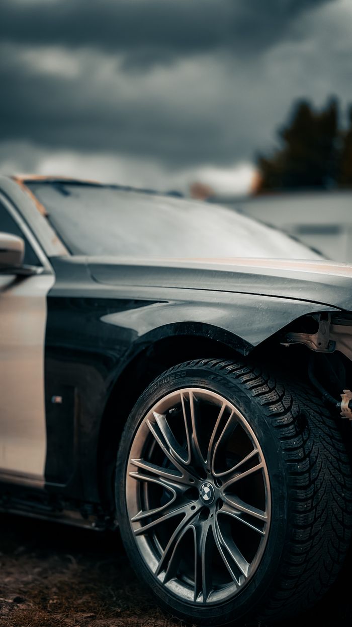 Detailed view of a car's front tire and body against a dramatic cloudy sky.