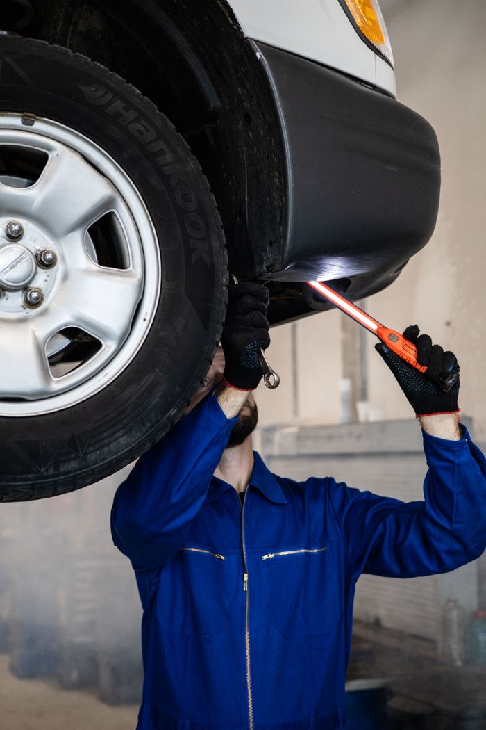 why-choose-us Mechanic inspecting a car in an auto repair shop, checking under the vehicle with a flashlight.